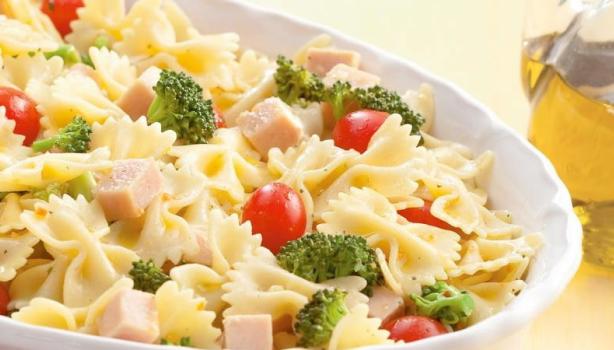 Receitas de saladas: Prato de salada de macarrão com brócolis, peito de peru e tomate cereja, ao lado tem uma garrafa com aze