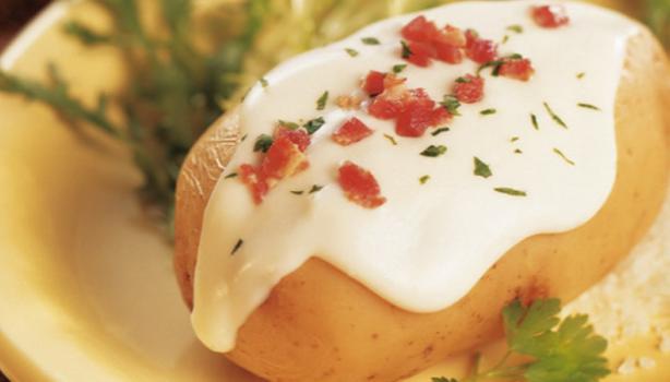 Prato com batata recheada e coberta por um molho branco e pedaços de tomate