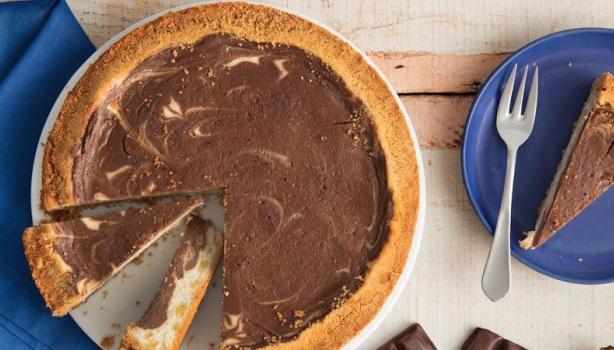 Torta de chocolate com dois pedaços cortados sobre um pano azul. À direita, pedaço de torta sobre um prato com um garfo ao la