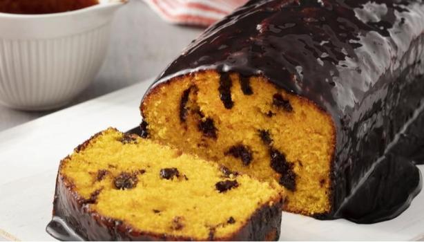 Bolo de cenoura com cobertura de chocolate em cima de um prato, à esquerda pote com gotas de chocolate