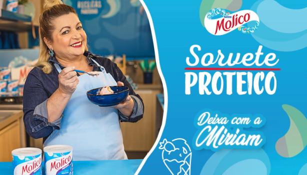 Imagem de uma mulher loira com um avental azul e a receita em mãos e à direita os dizeres com nome do programa e da receita