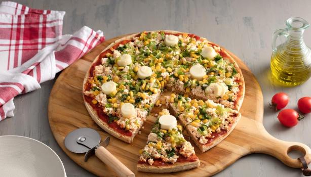 Pizza com duas fatias cortadas sobre uma tábua de madeira, abaixo da pizza tem um cortador e à direita azeite e dois tomates.