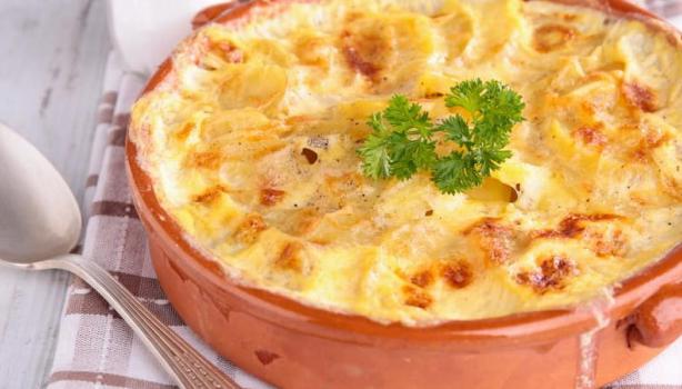 Imagem de uma travessa redonda com uma receita gratinada com queijo e uma folha de salsinha.