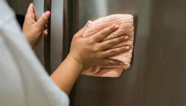 Mulher limpando a geladeira inox com um pano laranja