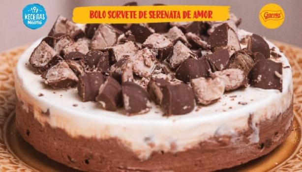 Fotografia de um bolo sorvete com camadas de chocolate na base e sorvete de creme no topo, decorado com pedaços de bombons co