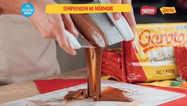 Temperagem no Mármore Imagem aproximada de chocolate derretido sendo derramado de um recipiente sobre uma placa de mármore com o título acima