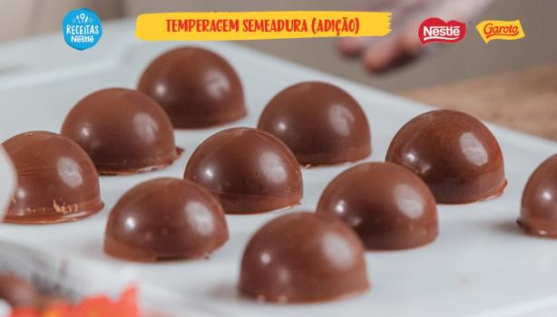 Temperagem por Adição ou Três Partes Imagem bastante aproximada de bombons caseiros de chocolate brilhantes sobre papel manteiga com o título do vídeo acima