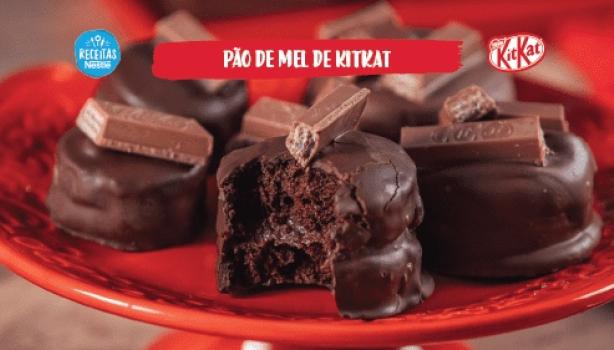 Fotografia mostra uma bancada de madeira e um prato vermelho redondo ao centro. Em cima, pães de mel de chocolate com KitKat.