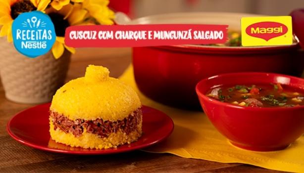 Fotografia mostra um cuscuz recheado com carne seca e um caldo com carnes, ambos em uma mesa de madeira e um pano amarelo.