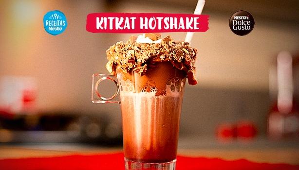 Imagem em tom vermelho com o KitKat Hotshake ao centro. Dentro de um copo está uma bebida com chocolate e crocantes de KitKat