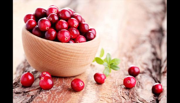 Tigela de madeira com cranberries frescos sobre superfície rústica, com algumas frutas espalhadas ao redor.