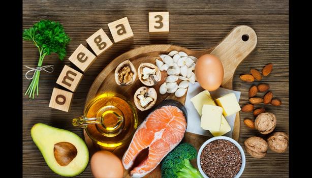 Alimentos ricos em ômega-3 sobre uma tábua: salmão, abacate, ovos, oleaginosas, azeite, manteiga e brócolis.