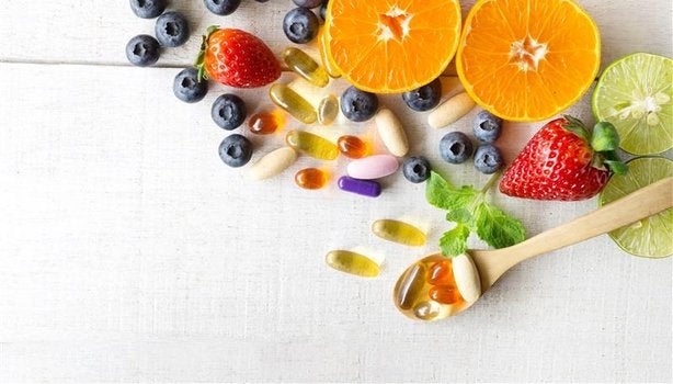 Frutas cítricas e vermelhas com cápsulas e comprimidos variados sobre fundo claro, representando vitaminas.