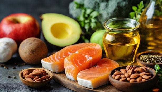 Salmão cru, azeite, abacate, maçã, nozes, amêndoas e brócolis sobre mesa rústica com fundo escuro.
