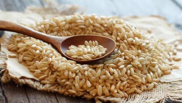 Arroz integral cru sobre tecido rústico, com colher de madeira apoiada por cima, em uma superfície de madeira envelhecida.