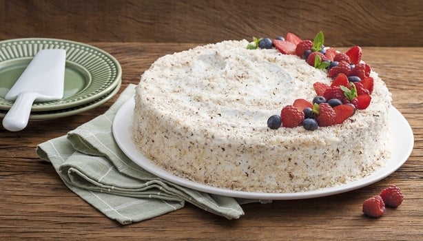 Imagem de um bolo redondo branco com coco decorado com frutas vermelhas.