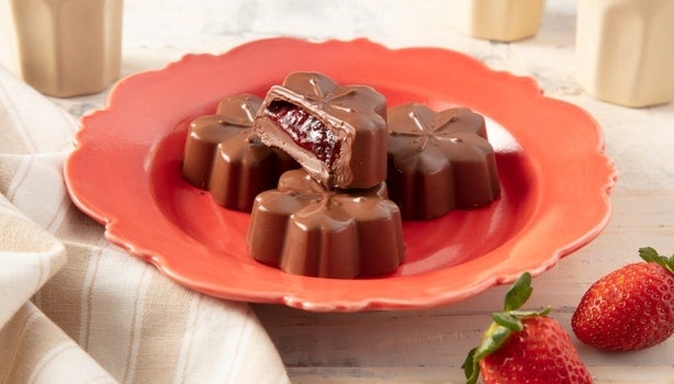 Imagem de bombons de chocolate em formato de flor com recheio de morango sobre um prato vermelho.