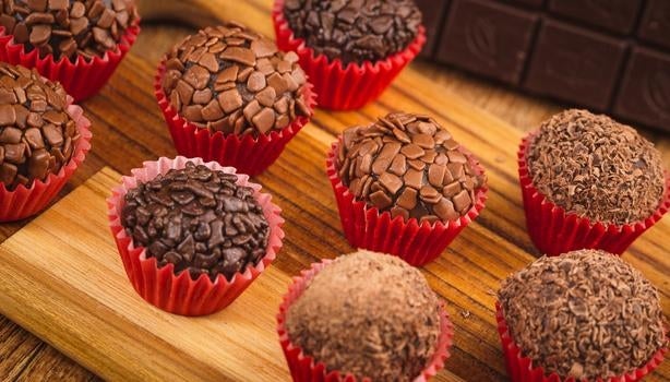 Imagem de brigadeiros de chocolate em forminhas vermelhas em uma tábua de madeira.