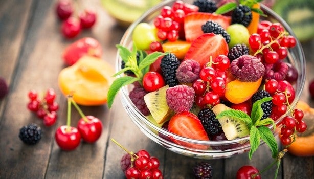 Tigela de vidro com frutas coloridas como framboesas, kiwis, cerejas, pêssego, groselha e amora.