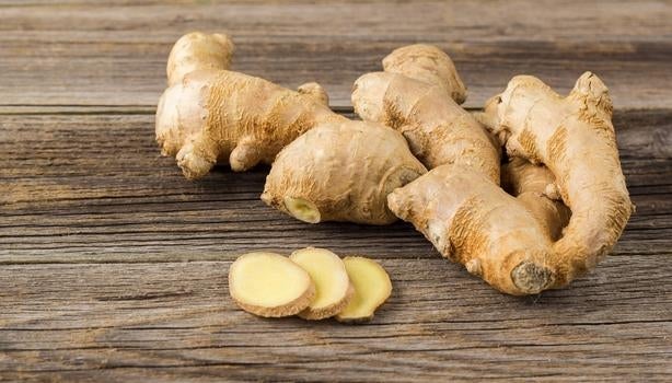 Raízes de gengibre frescas sobre superfície de madeira, com algumas fatias cortadas à frente.