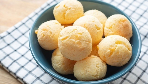 Imagem de um bowl azul com pães de queijo sobre um pano xadrez.