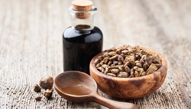 Frasco de vidro com própolis, tigela de madeira com pedaços de própolis e colher de madeira sobre superfície rústica.