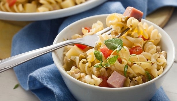 Imagem de um bowl branco com salada de macarrão parafuso com cubos de presunto, tomate e azeitonas.