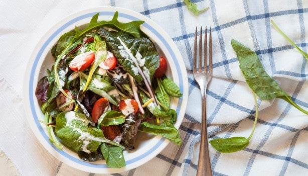 Bowl de salada verde com tomates e molho de iogurte sobre um pano xadrez branco e azul.