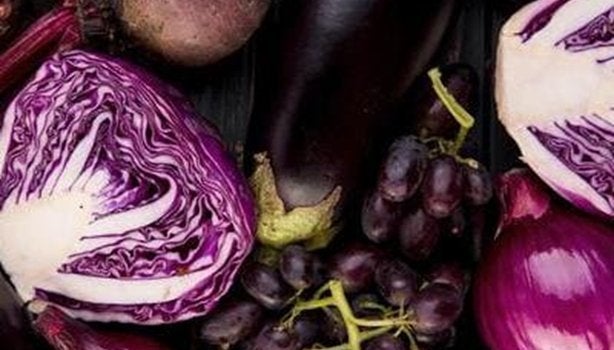 Alimentos roxos, incluindo legumes e frutas como cebola, berinjela, repolho e beterraba misturados em cima de uma mesa.