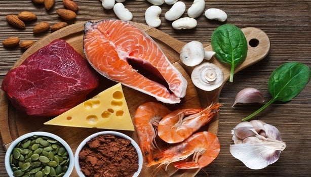 Variedade de alimentos ricos em zinco, incluindo carne, salmão, camarão, queijo, sementes, cogumelos, alho e espinafre.