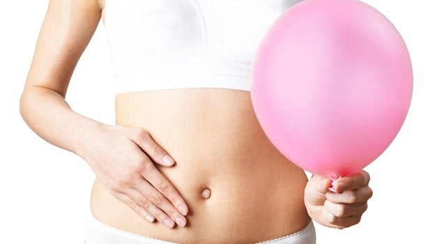 Mulher com a mão na barriga segurando um balão rosa representando barriga inchada.