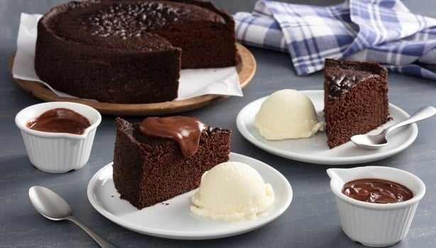 Bolo de chocolate servido com bolas de sorvete de creme e cobertura, acompanhado de pequenas tigelas com calda de chocolate.