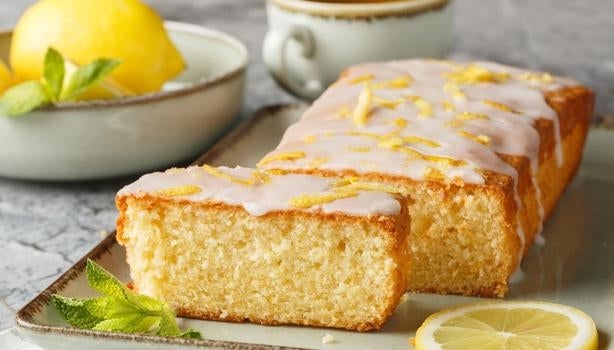 Bolo de limão com cobertura glaceada e raspas de limão, servido em fatias sobre bandeja com limão fresco ao lado.