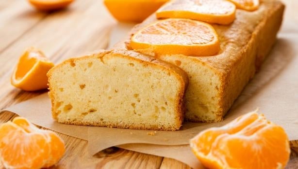 Bolo retangular de tangerina com gomos de tangerina e uma fatia cortada.
