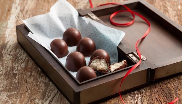 Bombons de chocolate com recheio de coco em caixa de madeira decorada com fita vermelha.