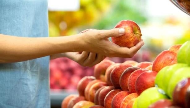 Mão segurando uma maçã como se estivesse escolhendo frutas.