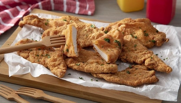 Filés de frango empanados e fritos, servidos em tábua de madeira com garfos de madeira e tempero verde por cima.