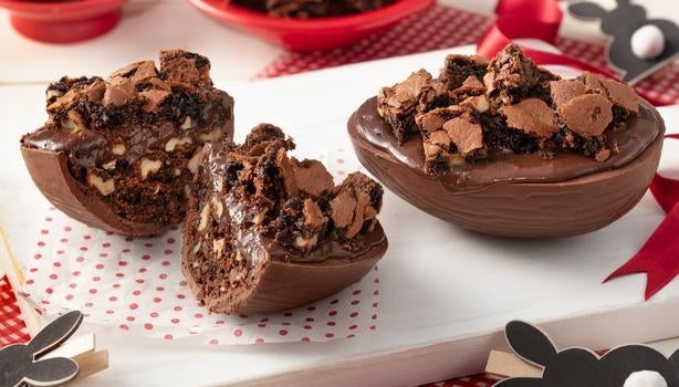 Ovo de Páscoa de chocolate recheado com brownie e pedaços crocantes decorado em uma bandeja branca.