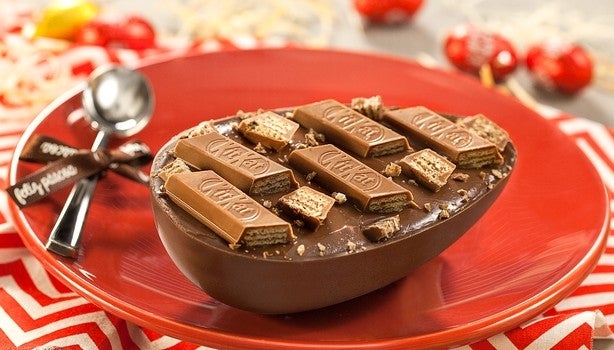 Ovo de Páscoa de chocolate ao leite decorado com pedaços de KitKat, servido em prato vermelho.