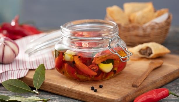 Pimenta em conserva caseira com alho e azeite em pote de vidro sobre tábua de madeira.