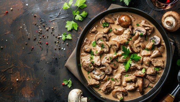 Prato de strogonoff de carne com cogumelos fatiados em molho cremoso, decorado com salsa fresca.
