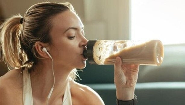 Mulher com roupas de ginástica bebendo um smoothie. A imagem representa os suplementos proteicos.