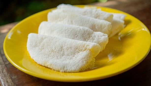 Tapiocas brancas dobradas servidas em prato amarelo sobre mesa de madeira.