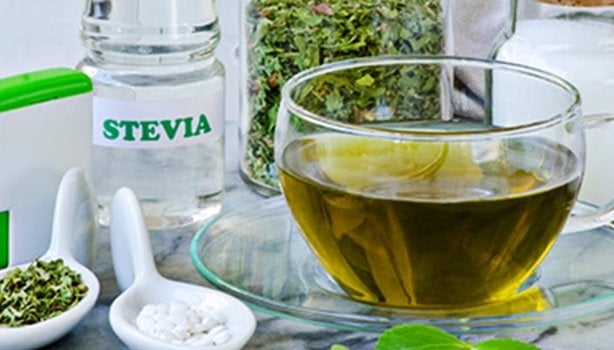 Uma xícara com chá, rodeada por folhas, ervas e especiarias, além de tipos de adoçantes - como a stevia. 