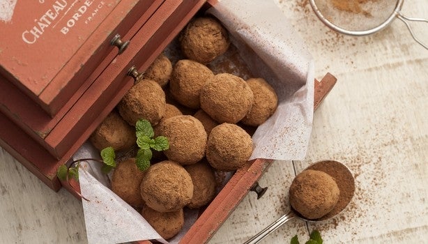 Trufas de chocolate polvilhadas com cacau em pó, servidas em caixa rústica de madeira, com toque de folhas de hortelã.