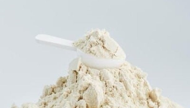 Whey protein em pó em cima de uma mesa branca, junto a um scoop. A imagem representa se whey substitui refeição.