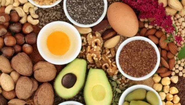 Vista superior de alimentos saudáveis como abacate, nozes, sementes, ovos e castanhas dispostos em tigelas.