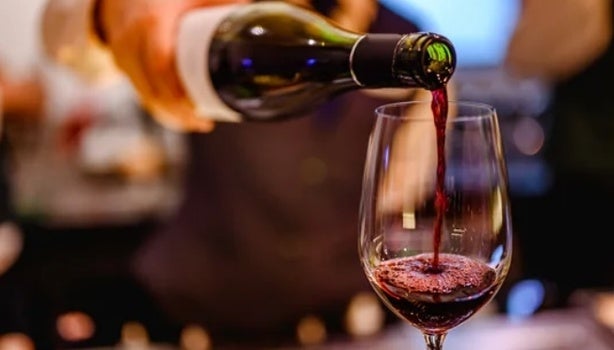 Vinho tinto sendo servido em taça de vidro, com fundo desfocado, representando os benefícios do vinho.