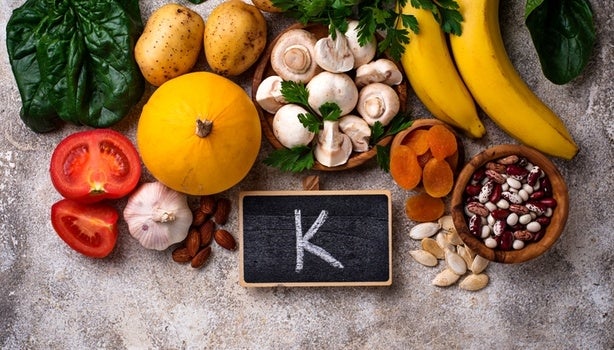 Alguns alimentos ricos em potássio, junto a um quadro negro com a letra K desenhada, representando potássio para que serve.