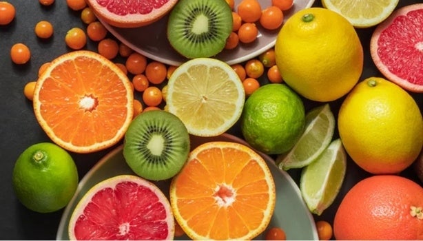 Frutas cítricas variadas como laranja, limão, kiwi e grapefruit cortadas ao meio, dispostas em fundo escuro.